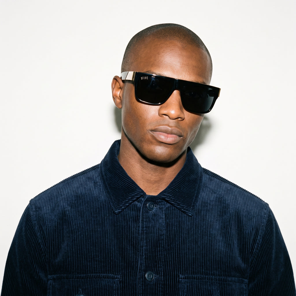 Man wearing dark sunglasses and a navy blue corduroy shirt against a white background [g:black s:all o:3]