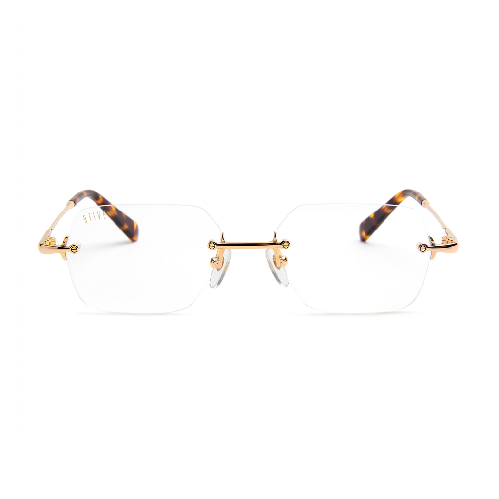 Rimless eyeglasses with clear lenses, gold metal bridge and hinge details, and tortoiseshell temples on a white background.