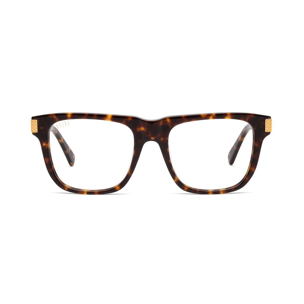 A pair of square-frame eyeglasses with a classic tortoiseshell pattern in brown and black, featuring small gold metal accents on the temples, shown against a plain white background. [g:clear s:all o:1]
