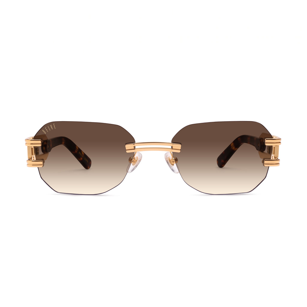 A pair of Rimless sunglasses with a gold metal frame, gradient brown lenses, and tortoiseshell temple arms, shown against a plain white background. [g:brown-gradient s:all o:1]
