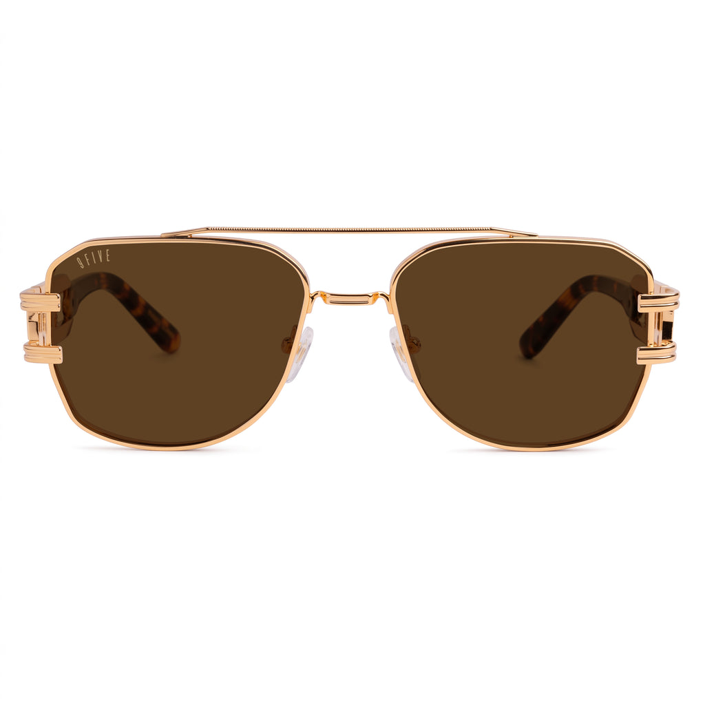A pair of angular aviator-style sunglasses with a rose gold metal frame, brown lenses, and tortoiseshell temple arms, shown against a plain white background. [g:brown s:all o:1]