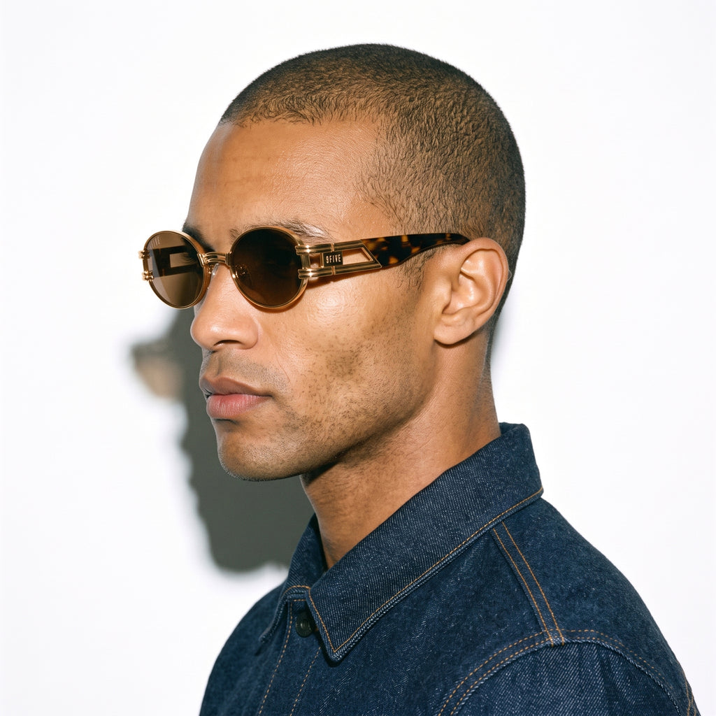 A man in profile wearing round tortoiseshell sunglasses with dark brown lenses and a dark blue denim shirt, set against a plain white background.
[g:brown s:all o:3]
